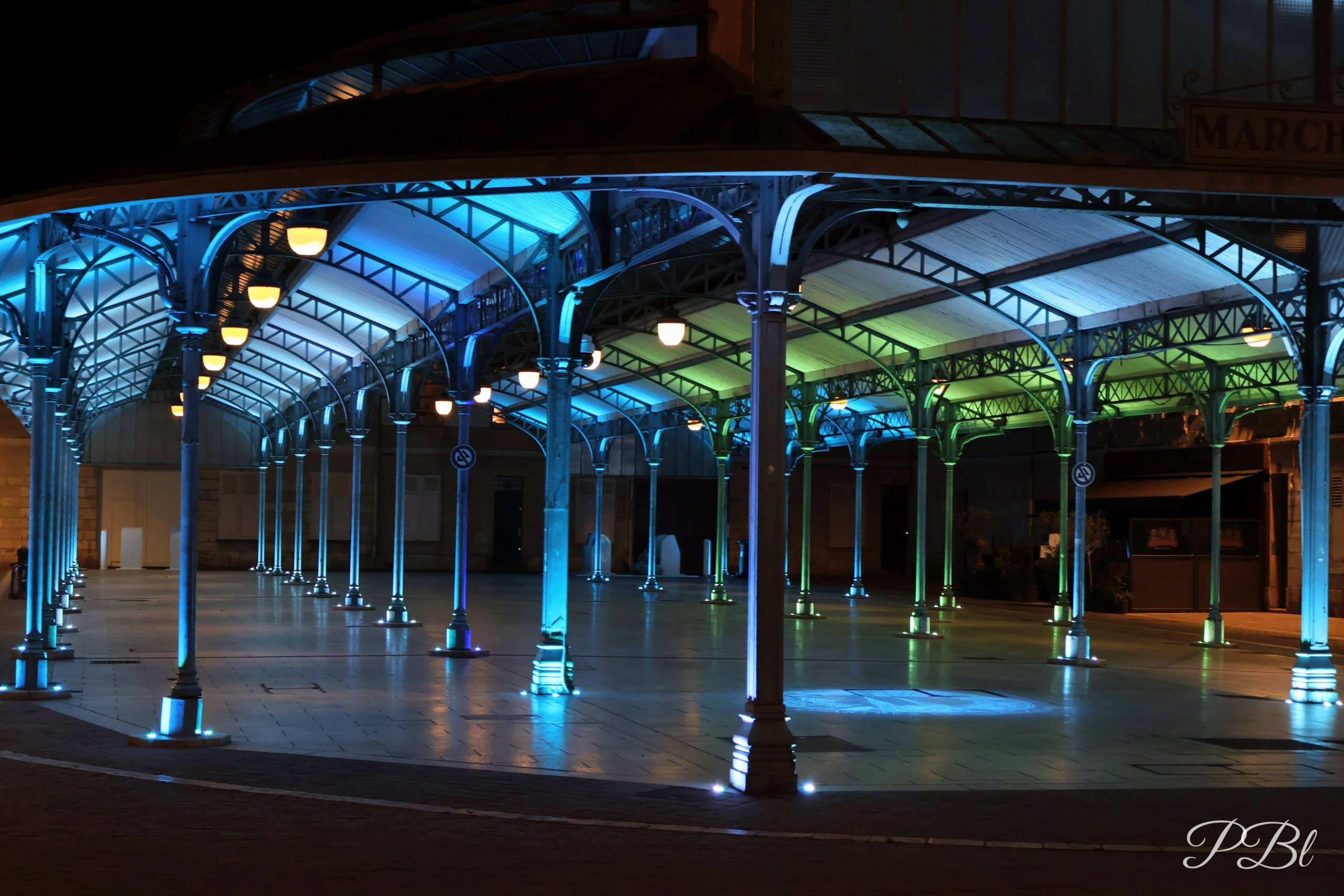 Halle de marché à charpente métallique illuminée de bleu, la nuit