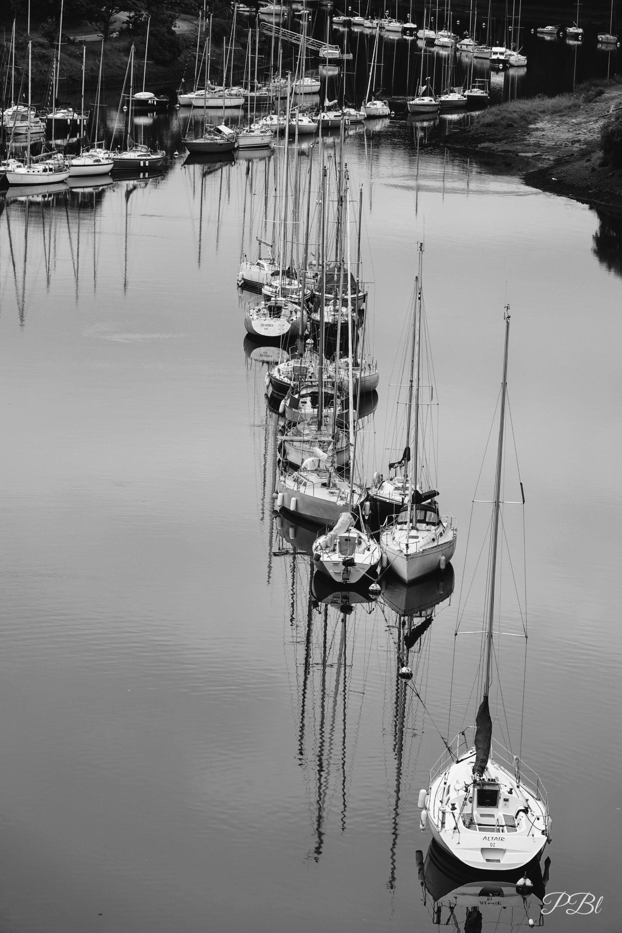 Voiliers alignés dans un estuaire, en noir et blanc