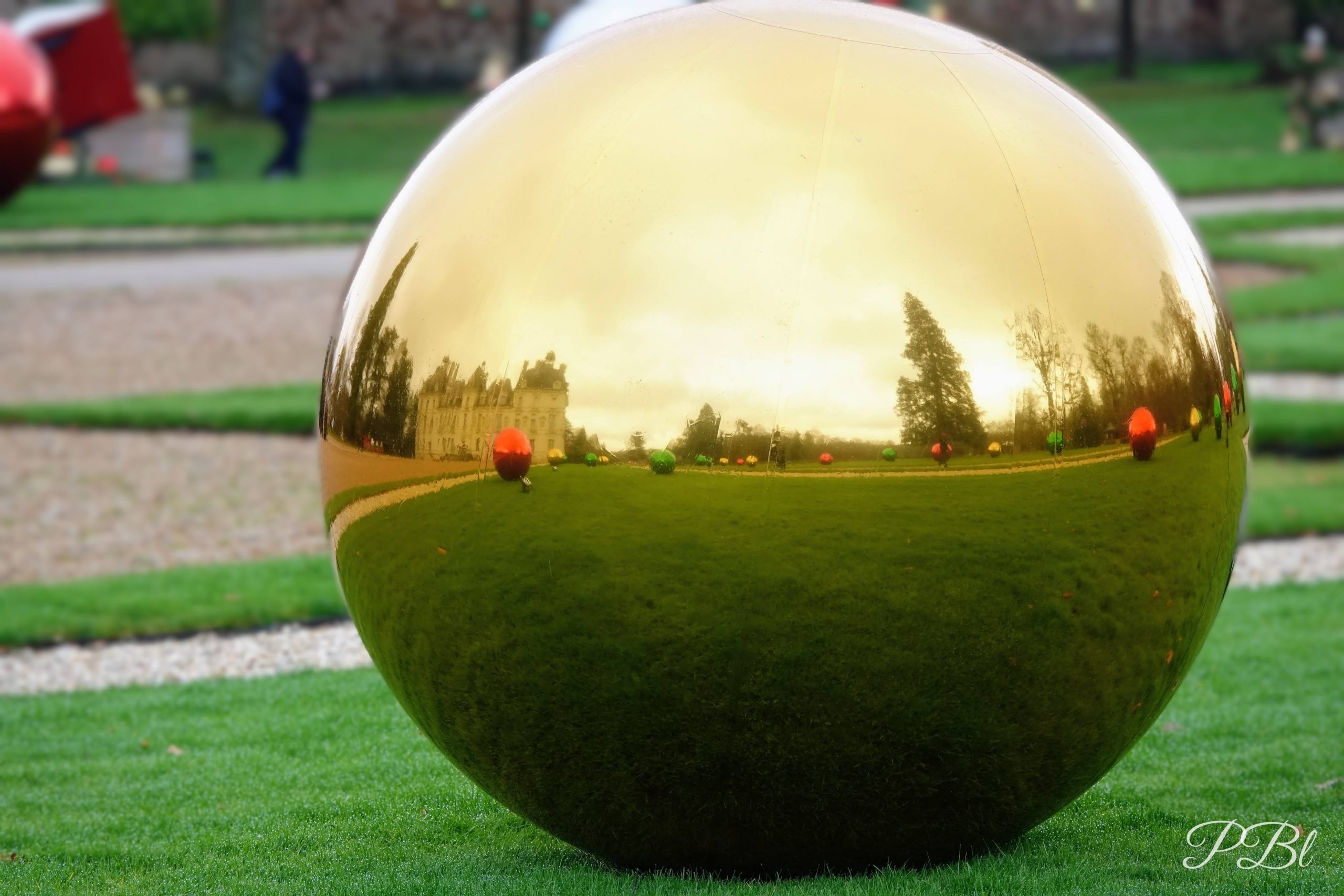 Grande sphère dorée sur une pelouse, reflétant un château et son jardin