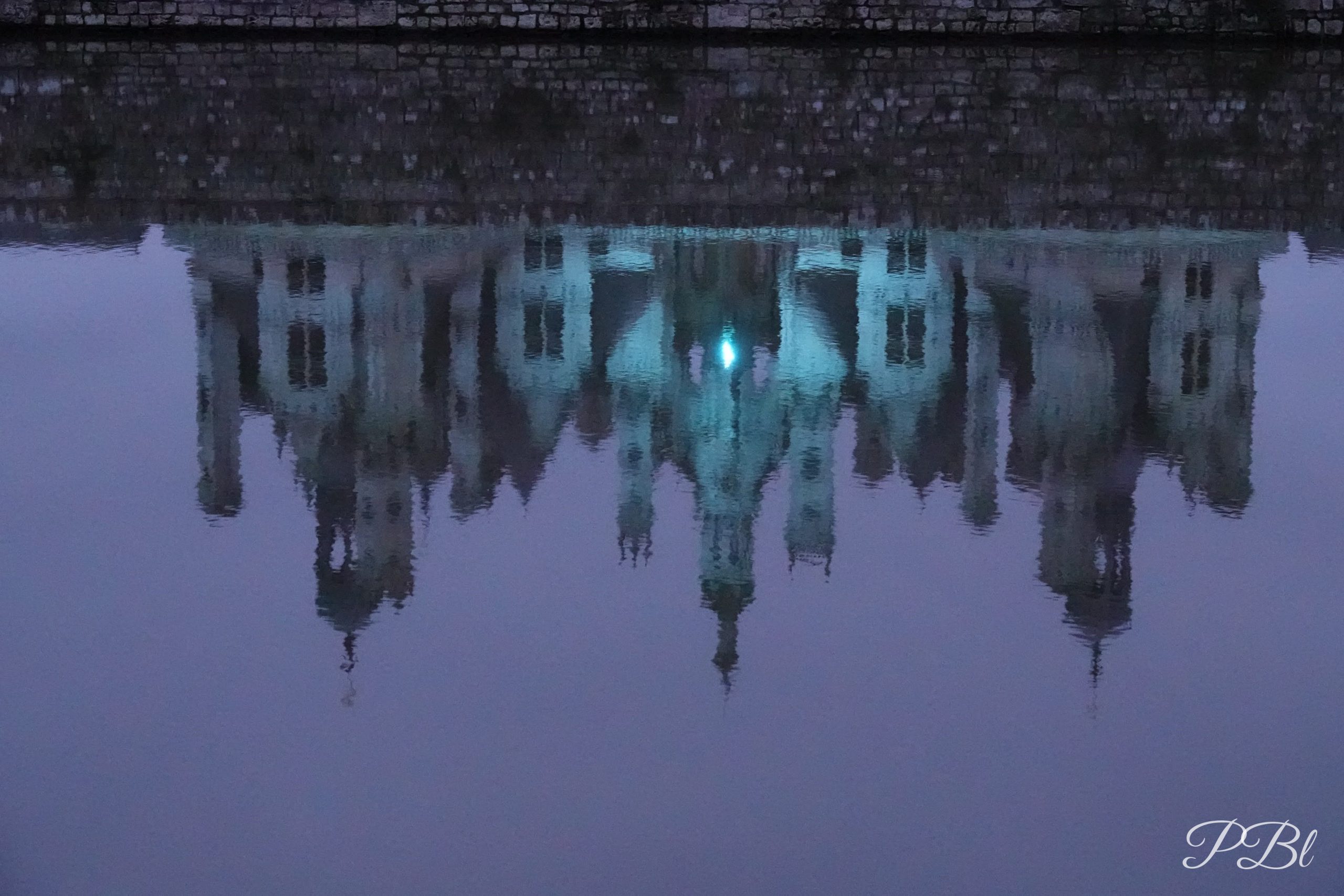 Reflet d'un château illuminé dans l'eau, à la tombée de la nuit